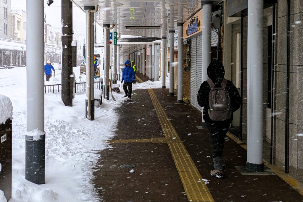 雪が降り続いている中、市内のアーケードを歩いている写真
