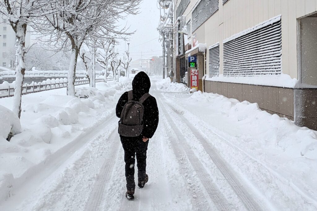 街中の雪が積もった道を黙々と歩いている相方の後ろ姿の写真
